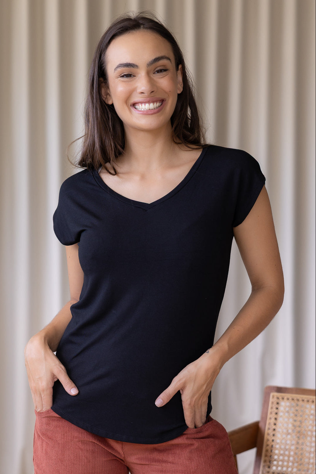 Woman wearing a black stretch rayon jersey t-shirt with a V-neck and cap sleeves, with hands in pants pockets