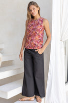 Woman standing in sun wearing black cotton pants paired with sleeveless floral cotton top with high round neckline