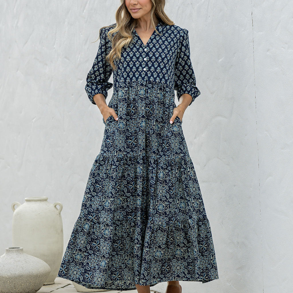 Woman poses in navy blue based floral cotton maxi dress with buttoned bodice, 3/4 sleeves and flowy three tiered maxi skirt