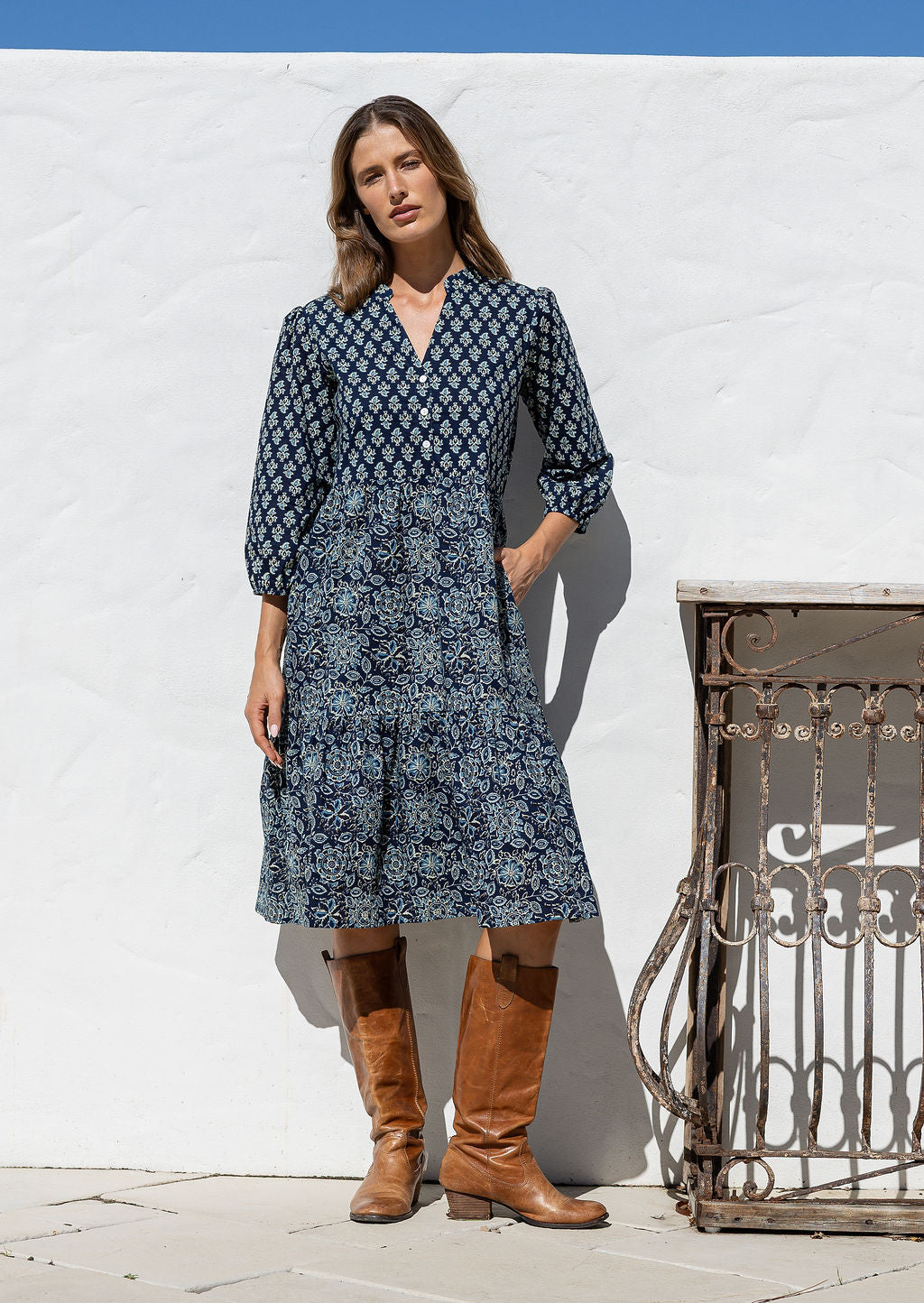 Woman standing in cotton tiered over the knee dress with 3/4 sleeves, buttoned bodice, V-neckline and one hand in pocket
