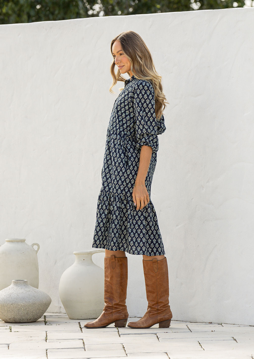Model stands side on in cotton over the knee length relaxed fit dress with 3/4 sleeves, paired with tan sandals