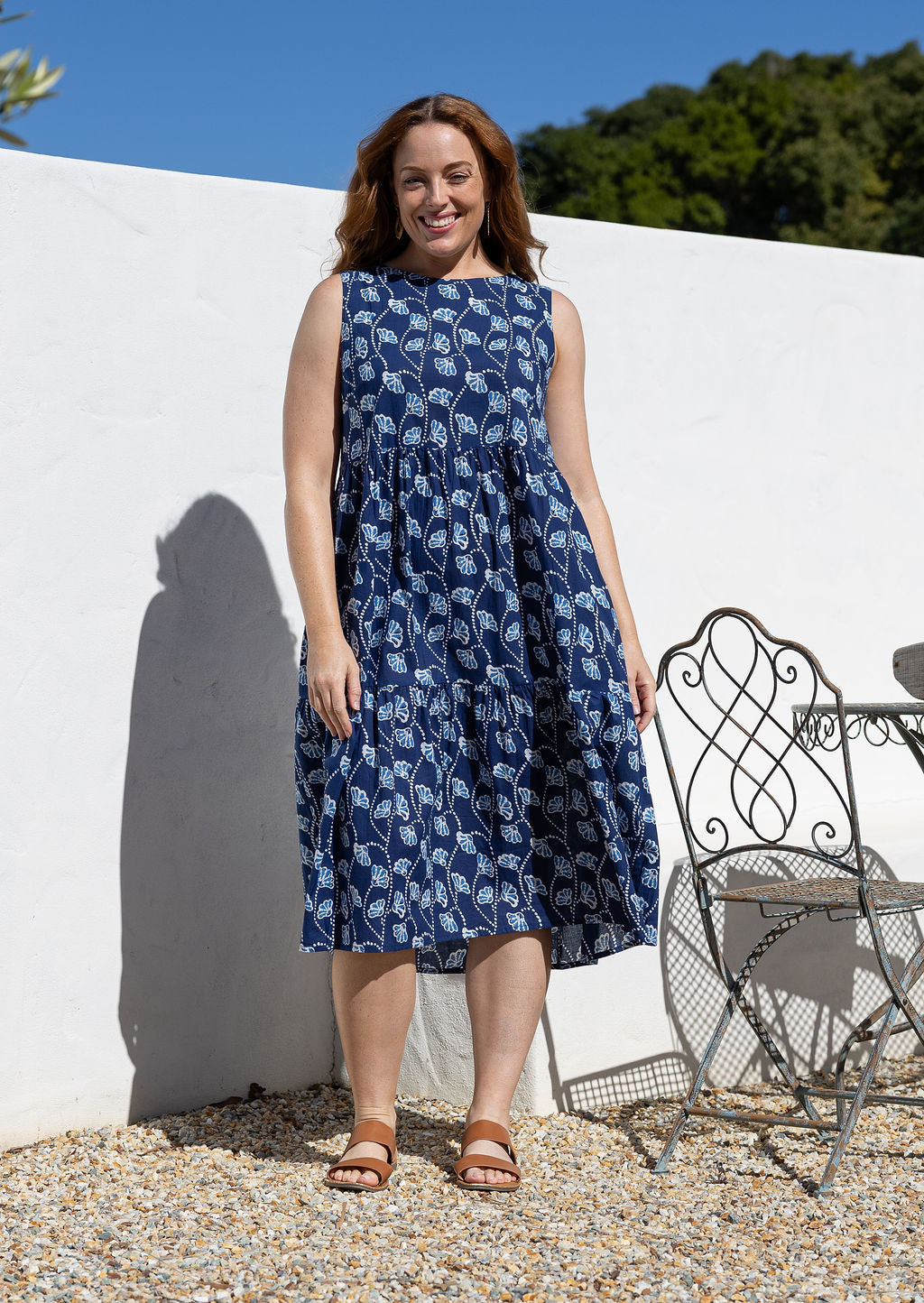 Woman in 100 percent cotton relaxed fit sleeveless dress with high round neckline, pockets and tiered style.