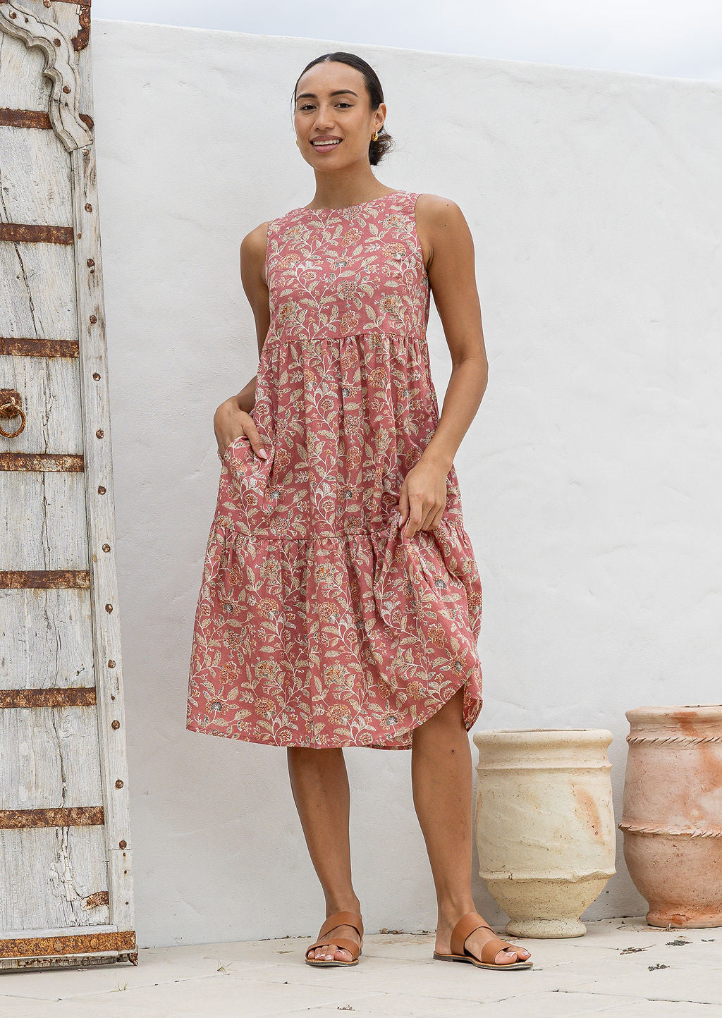 Woman in 100 percent cotton relaxed fit sleeveless dress with high round neckline, pockets and tiered style.