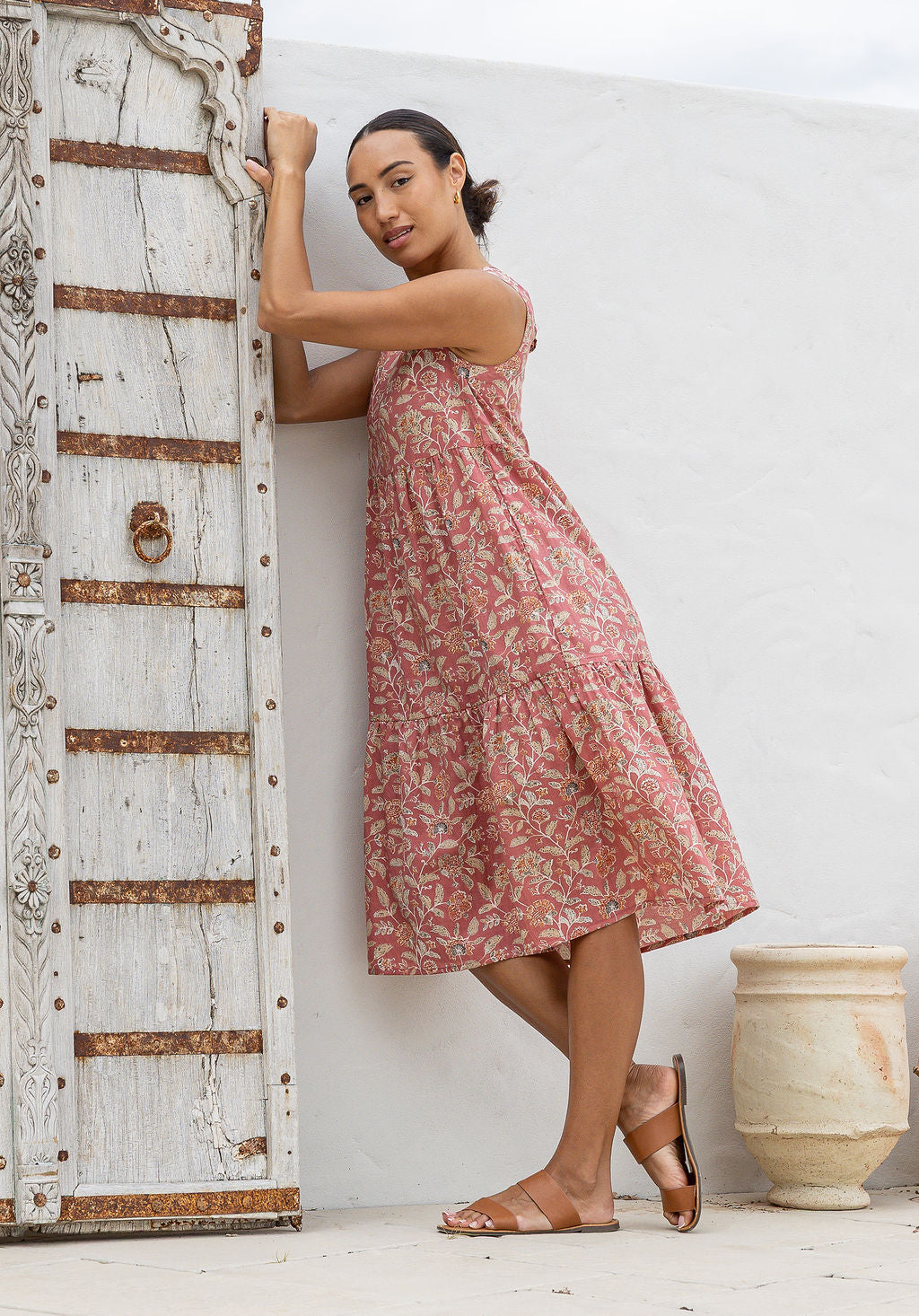 Woman stands in side pose wearing a tiered sleeveless sundress with pockets, high round neck and empire waist.