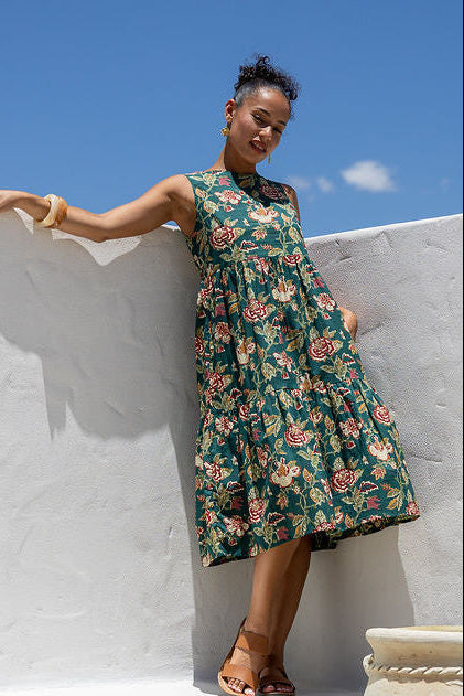 Woman in 100 percent cotton relaxed fit sleeveless dress with high round neckline, pockets and tiered style.