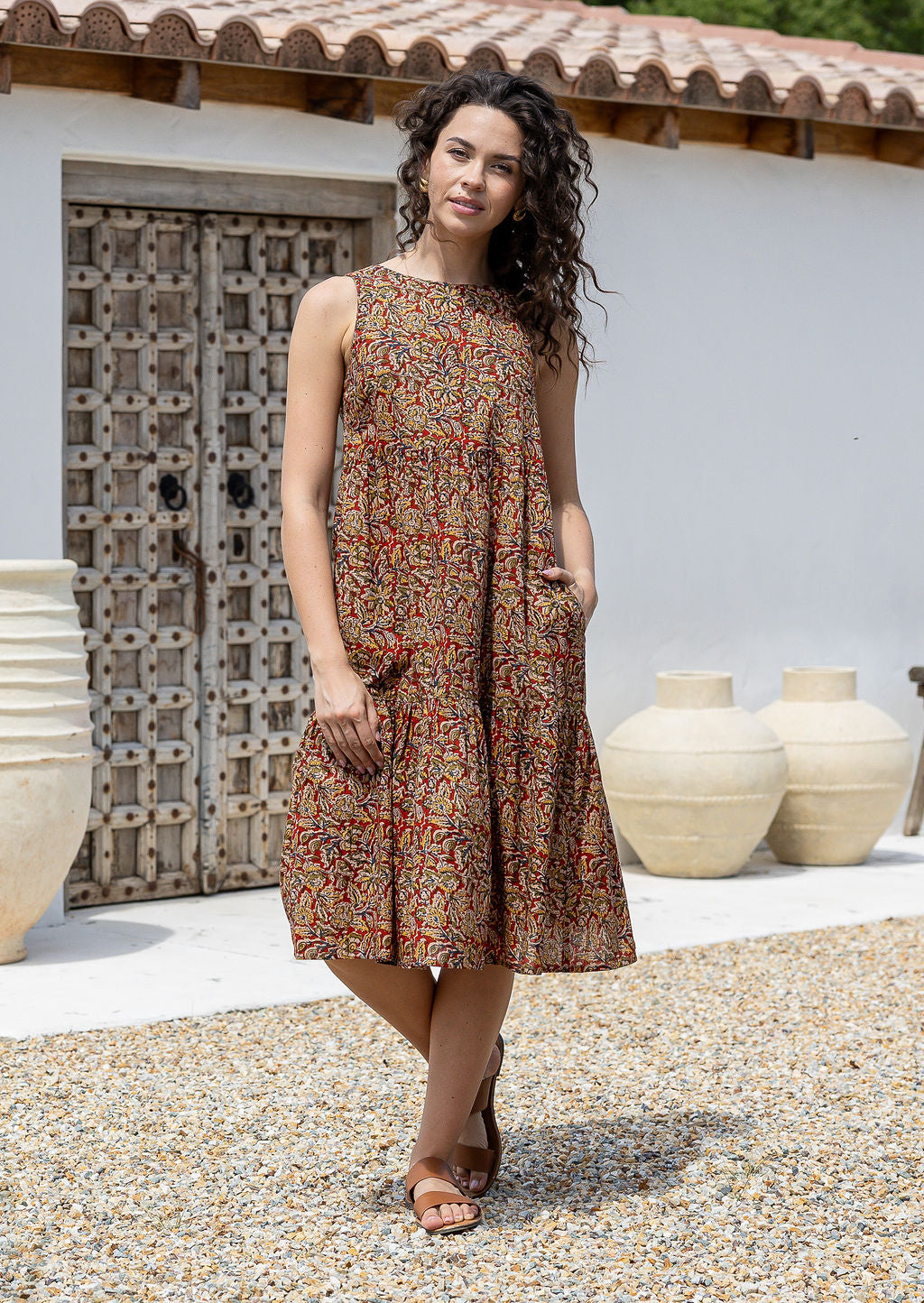 Woman wearing a Indian floral print cotton midi dress with one hand in pocket standing in front of a textured wall and white door.