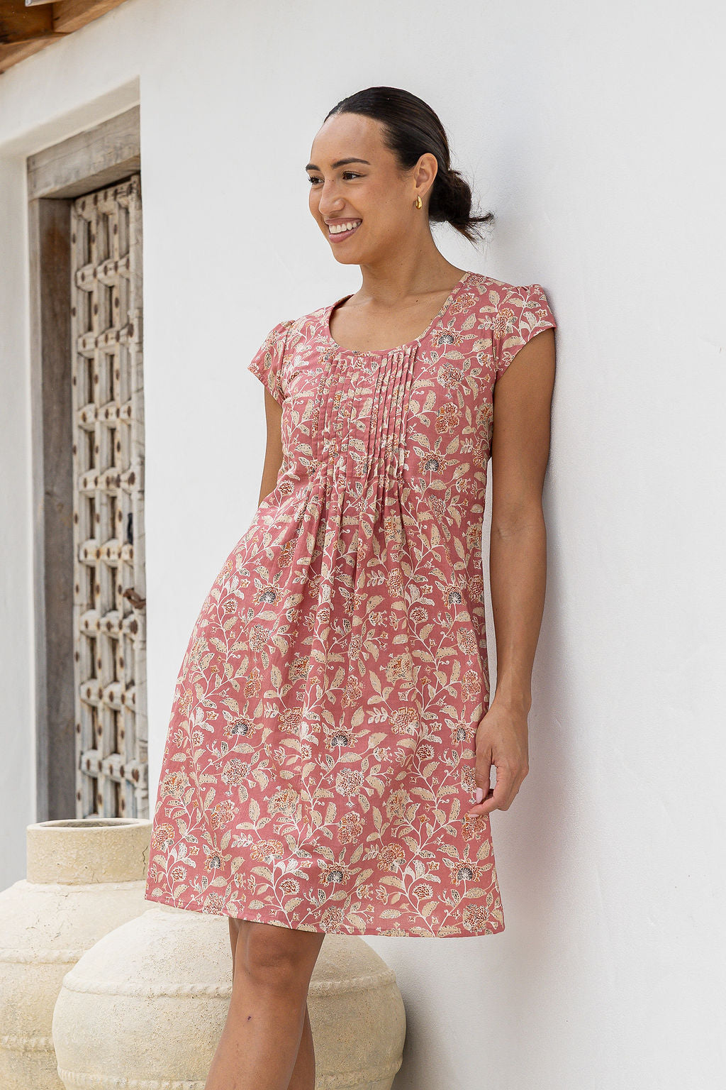 Woman wearing a 100% cotton rose pink based floral dress standing against a white wall.
