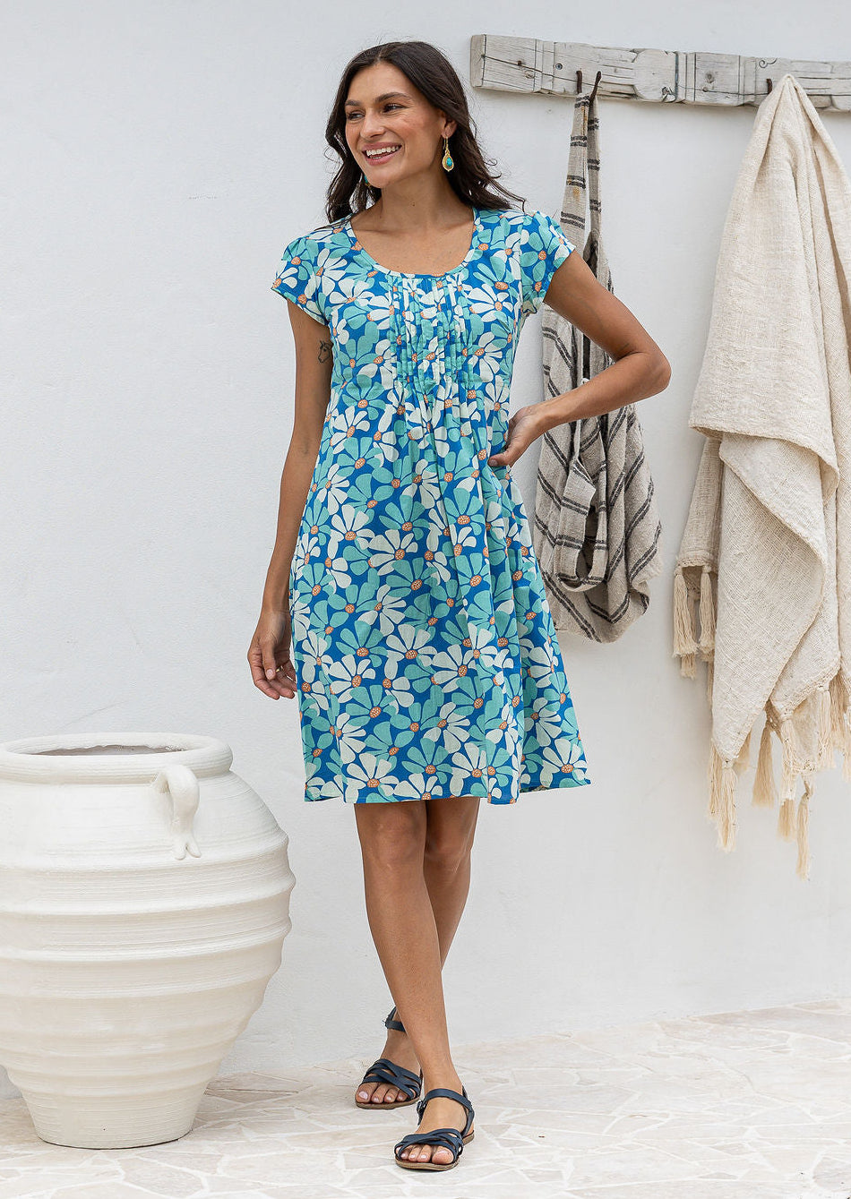 Woman posing in cap sleeved cotton above knee dress in blue and aqua daisy print, with hand on hip