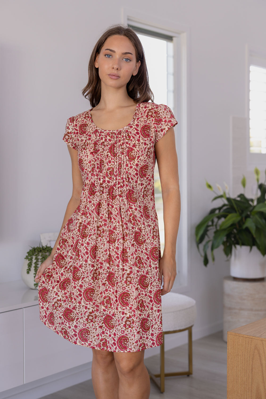 Woman wearing a 100% cotton floral dress in a bright room with white walls and a plant.