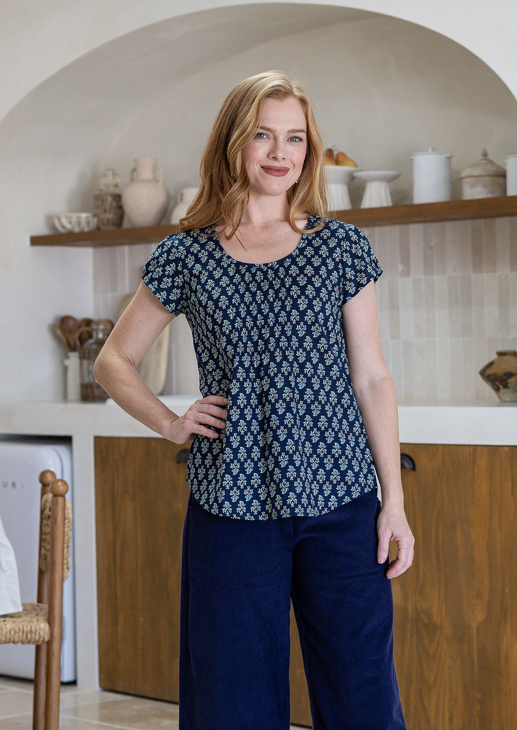 Woman wearing a blue floral top and plain pants in a kitchen setting