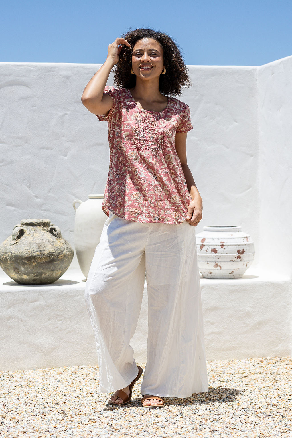Woman wears rose pink based floral print 100% cotton cap sleeve top with pin tuck detail across the bust and a scoop neckline