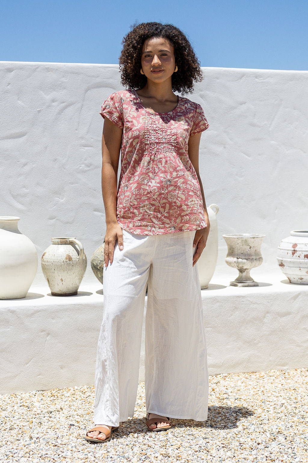 Woman wearing a rose pink based floral print short sleeve top with scoop round neckline and pleated detail across the bodice