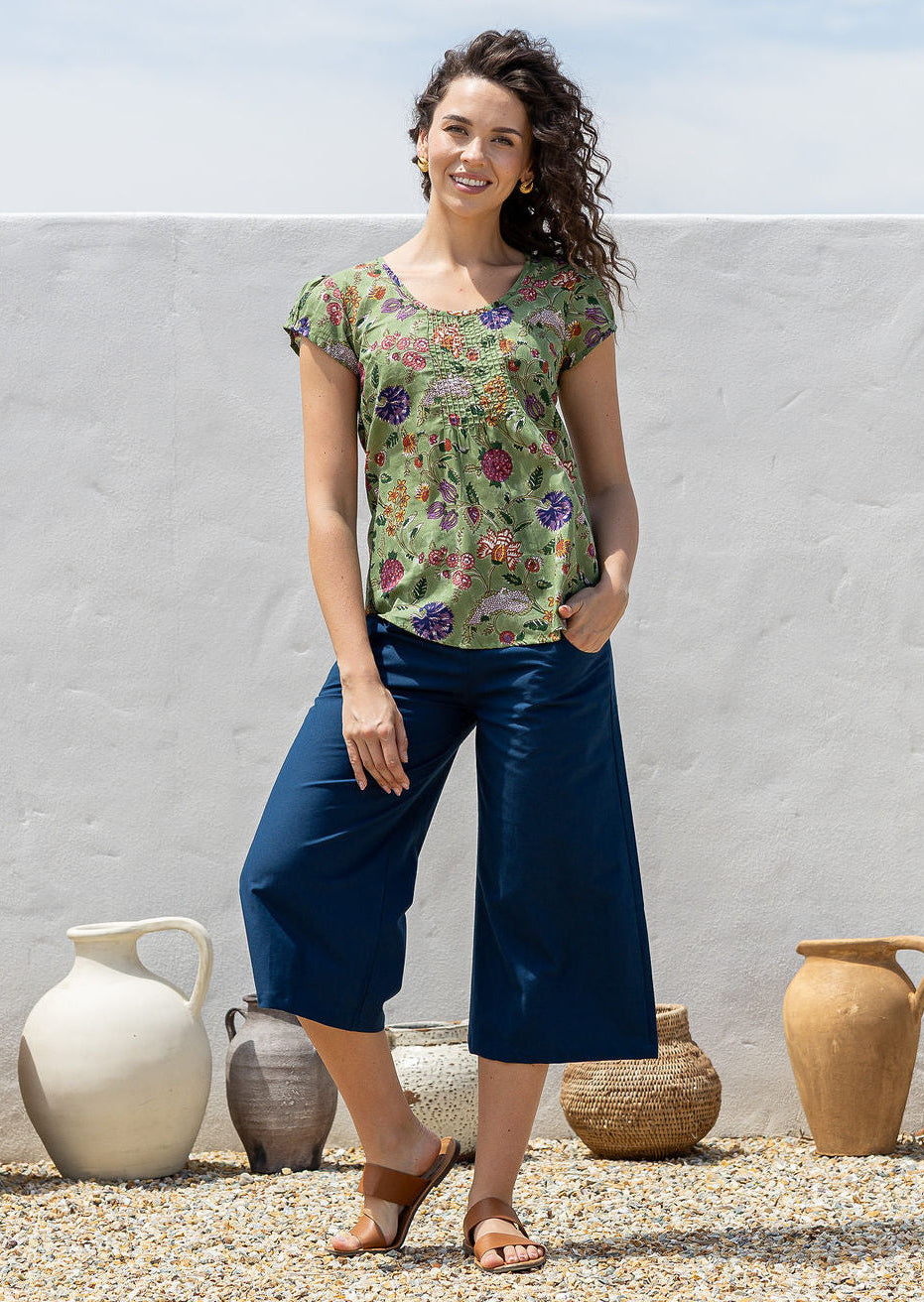 Woman wearing a moss green based floral print short sleeve top with scoop round neckline and pleated detail across the bodice