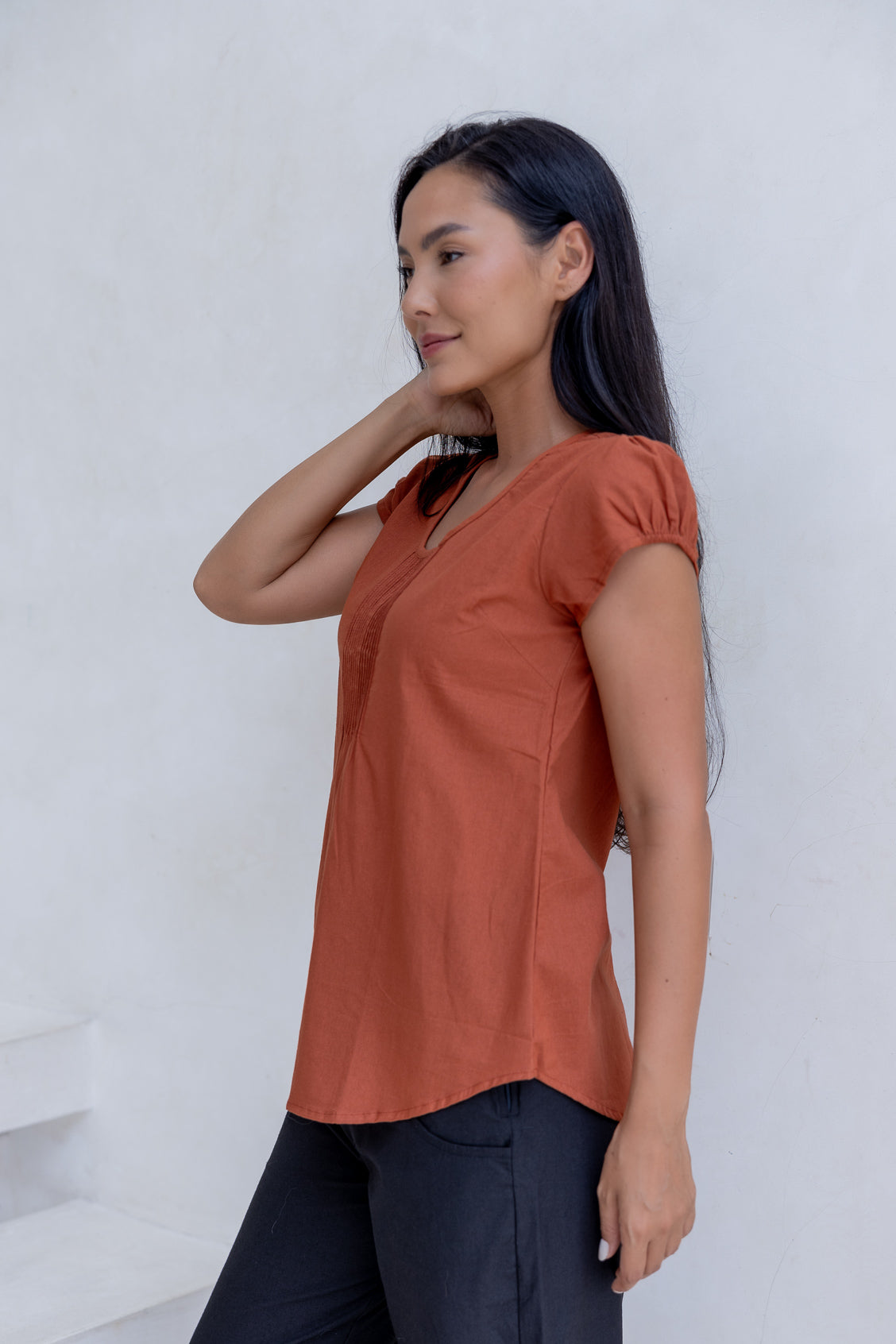 Woman wearing a rust-colored cotton top with cap sleeves and round neckline, against a white background