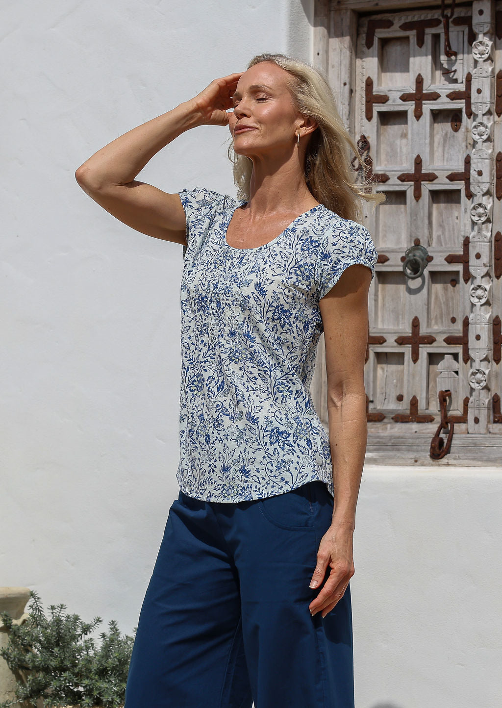 Woman wears 100% cotton short cap sleeved top with round neckline in white based blue floral print and lemon yellow highlights.