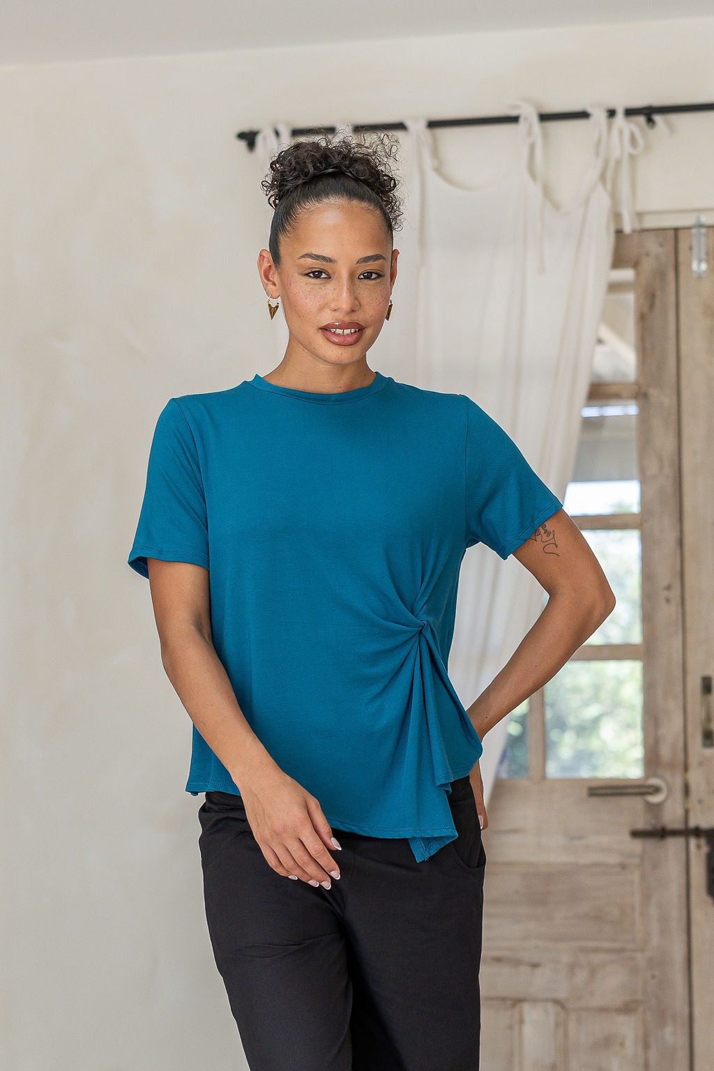 Woman wearing teal crew-neck T-shirt with twist knot front, stretch rayon jersey short-sleeve top in a casual setting