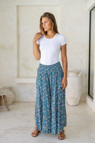 Woman standing in flowy, rayon wide leg pants in cerulean blue with smocked elastic waistban.