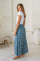 Woman wearing a white top and blue floral rayon pants with elasticated waistband in a minimalistic room.