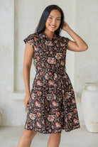 Woman wears fit and flare style shirt dress, 100% cotton with collar, cap sleeves, and removable waist tie in black based indian floral print.