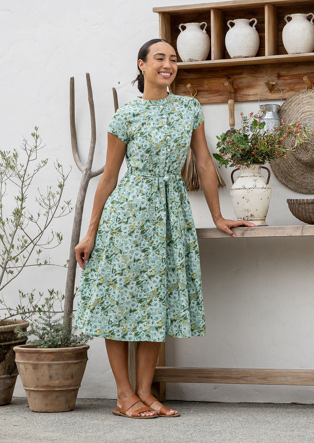 Woman wears retro style cotton button through midi length dress with high round neckline, short sleeves and a removable waist tie.