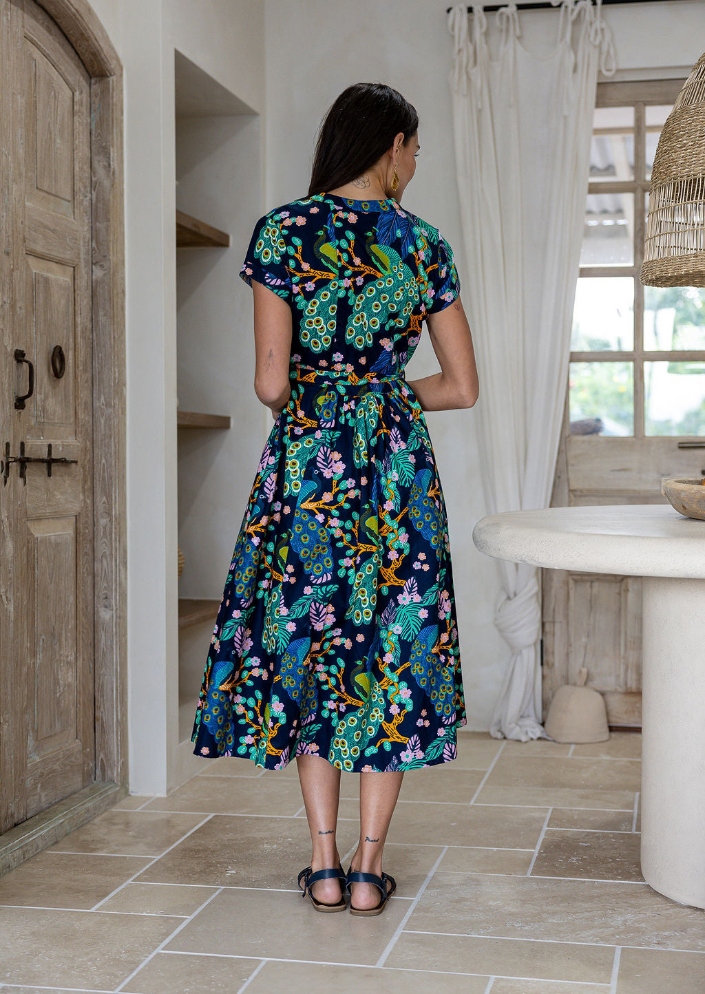 Woman standing backwards wearing a 1950's style short sleeved, button through cotton dress and high round neckline.