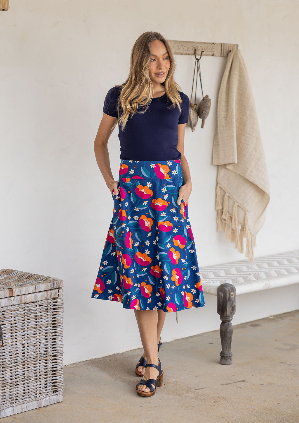 Woman is posing with both hand in pockets wearing a 100% cotton royal blue based floral print a line skirt.