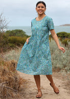 Model posing in knee length, 100% cotton dress in Indian floral print on aqua blue base.