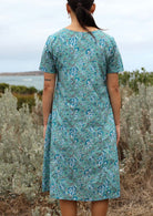 Model standing back wearing mid length cotton dress with relaxed fit and and  deep pockets.