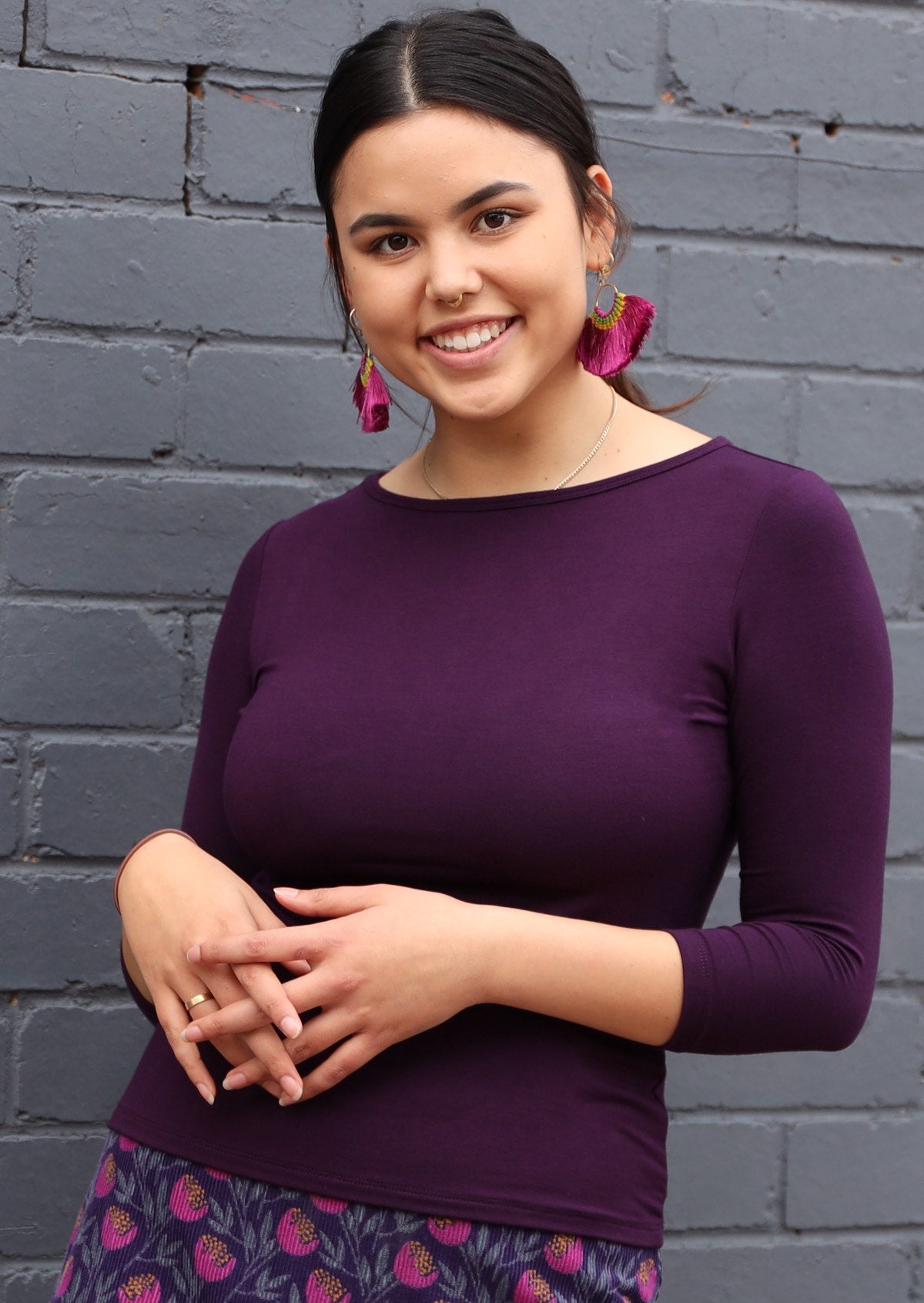 Woman with dark hair wearing a rayon boat neck purple 3/4 sleeve top.
