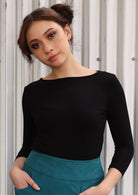 Woman wearing a rayon boat neck black 3/4 sleeve top with green skirt.