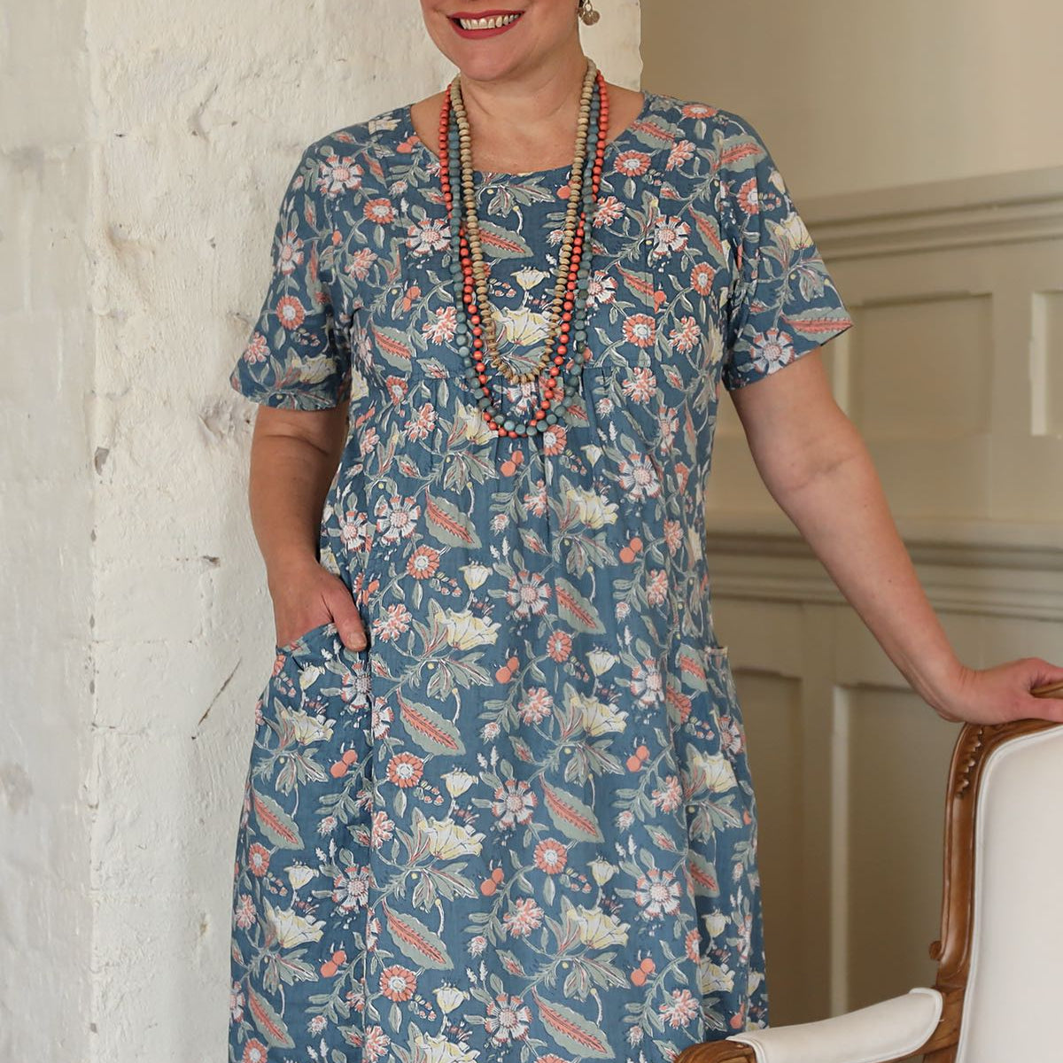 Woman wears floral print over the knee length cotton dress paired with wooden beaded necklaces
