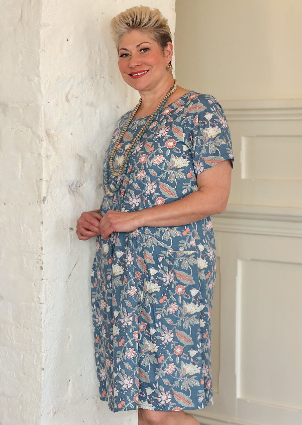 Model wears cotton knee length short sleeve dress with round neckline, in floral print on a mid blue base