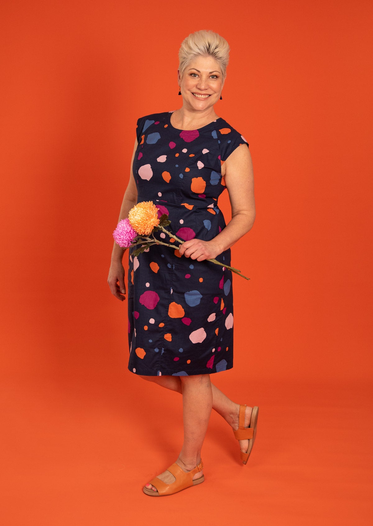 Woman wears retro style cotton dress with cap sleeves in colorful navy based print.
