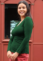 Woman with dark hair wearing a green long sleeve stretch v-neck soft rayon top.