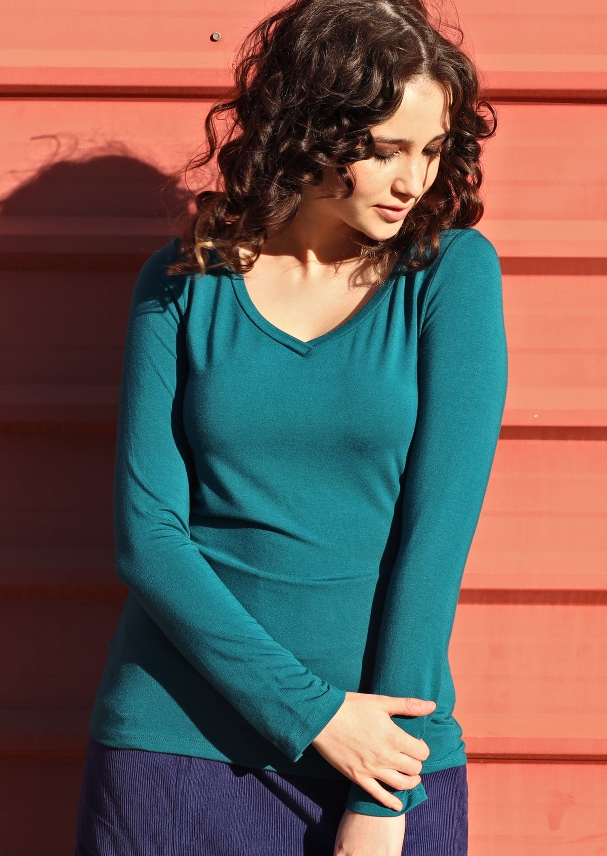 Woman wearing a teal long sleeve stretch v-neck soft rayon top with navy pants.