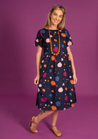 Woman stands wearing 100% cotton relaxed fit midlength dress.