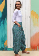Model standing slightly sideways in boho style cotton pants in aqua based indian floral print.