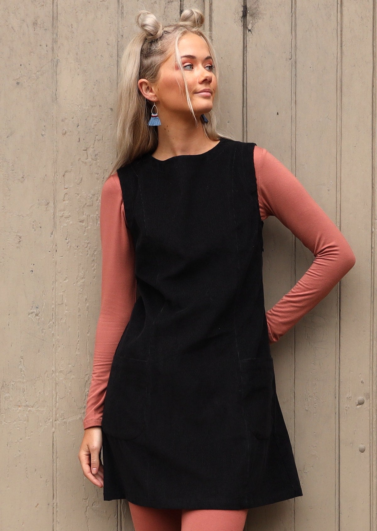 Woman poses in boat neck cotton corduroy sleeveless tunic dress with dusty pink top and leggings underneath