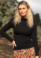 Woman wearing a turtle neck black fitted long sleeve soft stretch rayon top in front of trees.