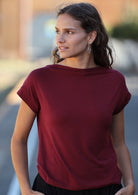 Woman wearing a wide neck mod maroon stretch rayon boat neck top with black pants.