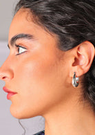 Model wears chunky silver tapered huggie earrings with hinged clasp