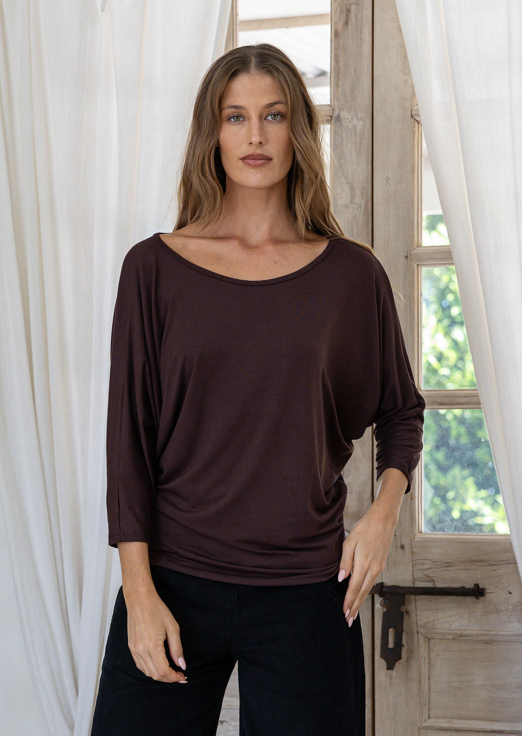 Woman wearing a brown rayon jersey batwing top with 3/4 sleeves and a wide round neckline, paired with black pants