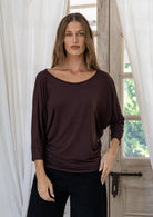 Woman wearing a brown rayon jersey batwing top with 3/4 sleeves and a wide round neckline, paired with black pants