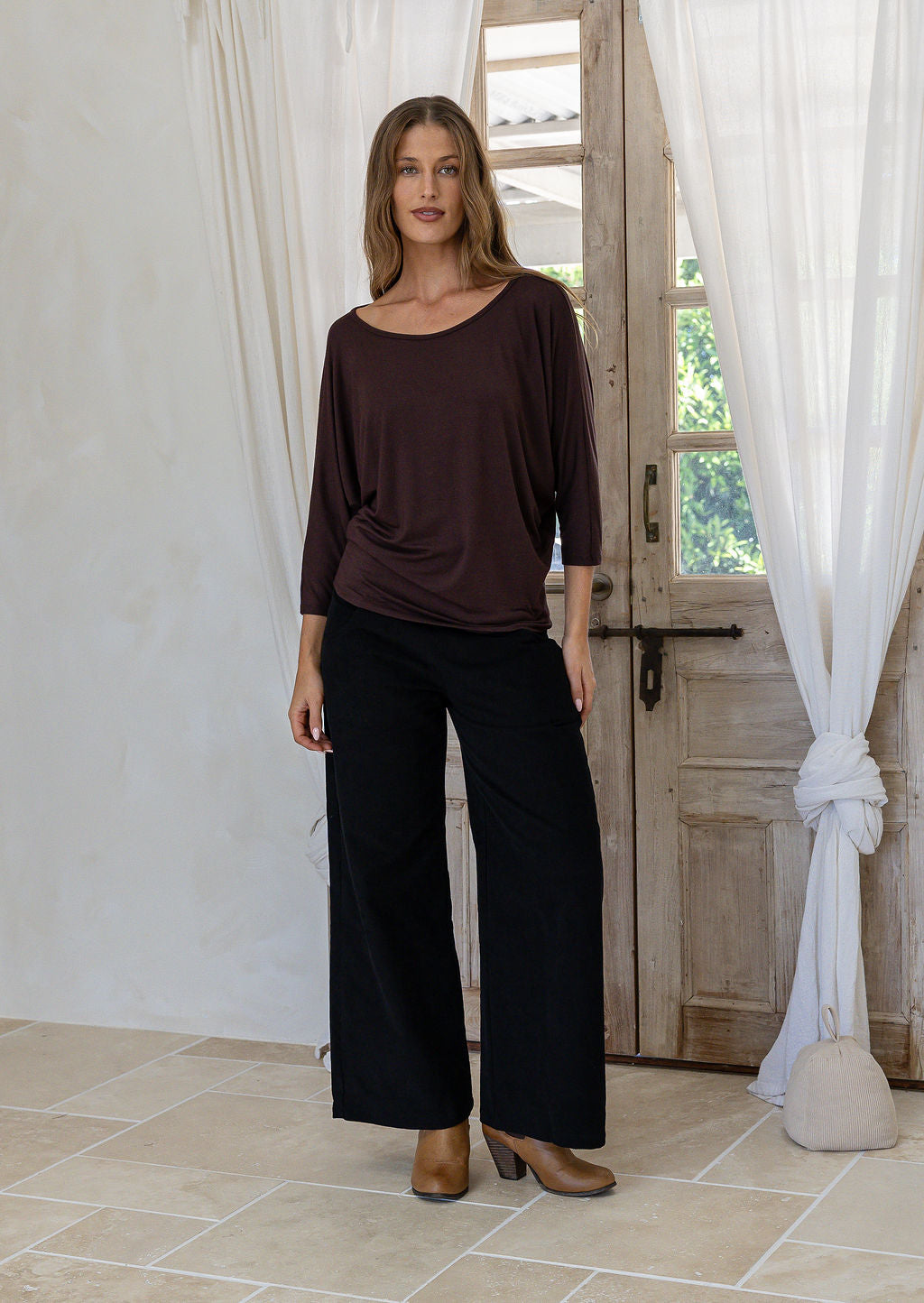 Woman wearing a brown rayon jersey batwing top with 3/4 sleeves and a round neckline, paired with black pants