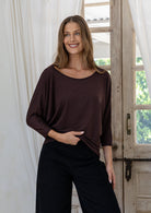 Woman wearing a brown rayon jersey batwing top with 3/4 sleeves and a round neckline, holding front of top