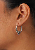 Woman wears silver hollow hoop earrings with an abundance of detail at the base