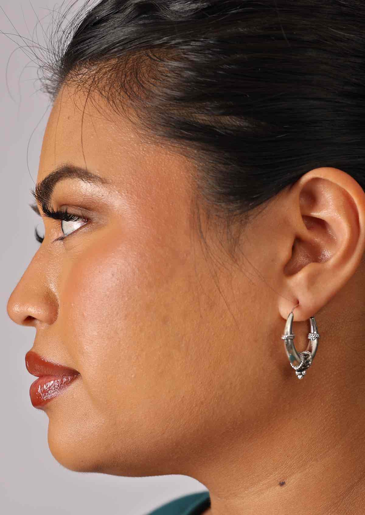 Woman wears silver tapered hollow hoop earrings with silver rope and bead details