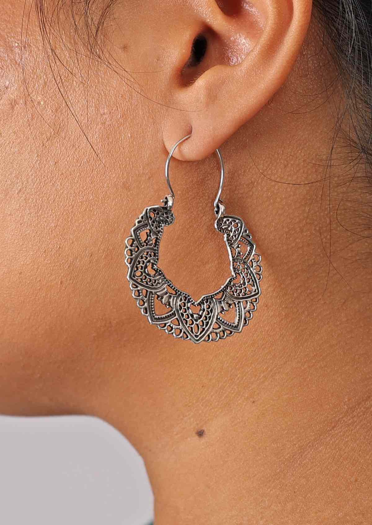 Close up of silver earrings boasting a delicate lace mandala design, with etched detail on one side