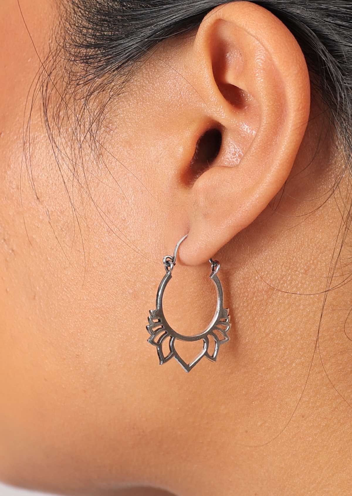 Close up of woman wearing sterling silver earring featuring a ring with cutout lotus petals emerging from the base, and secured with a wire hook