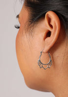 Woman wears sterling silver earrings featuring a ring with cutout lotus petals emerging from the base.